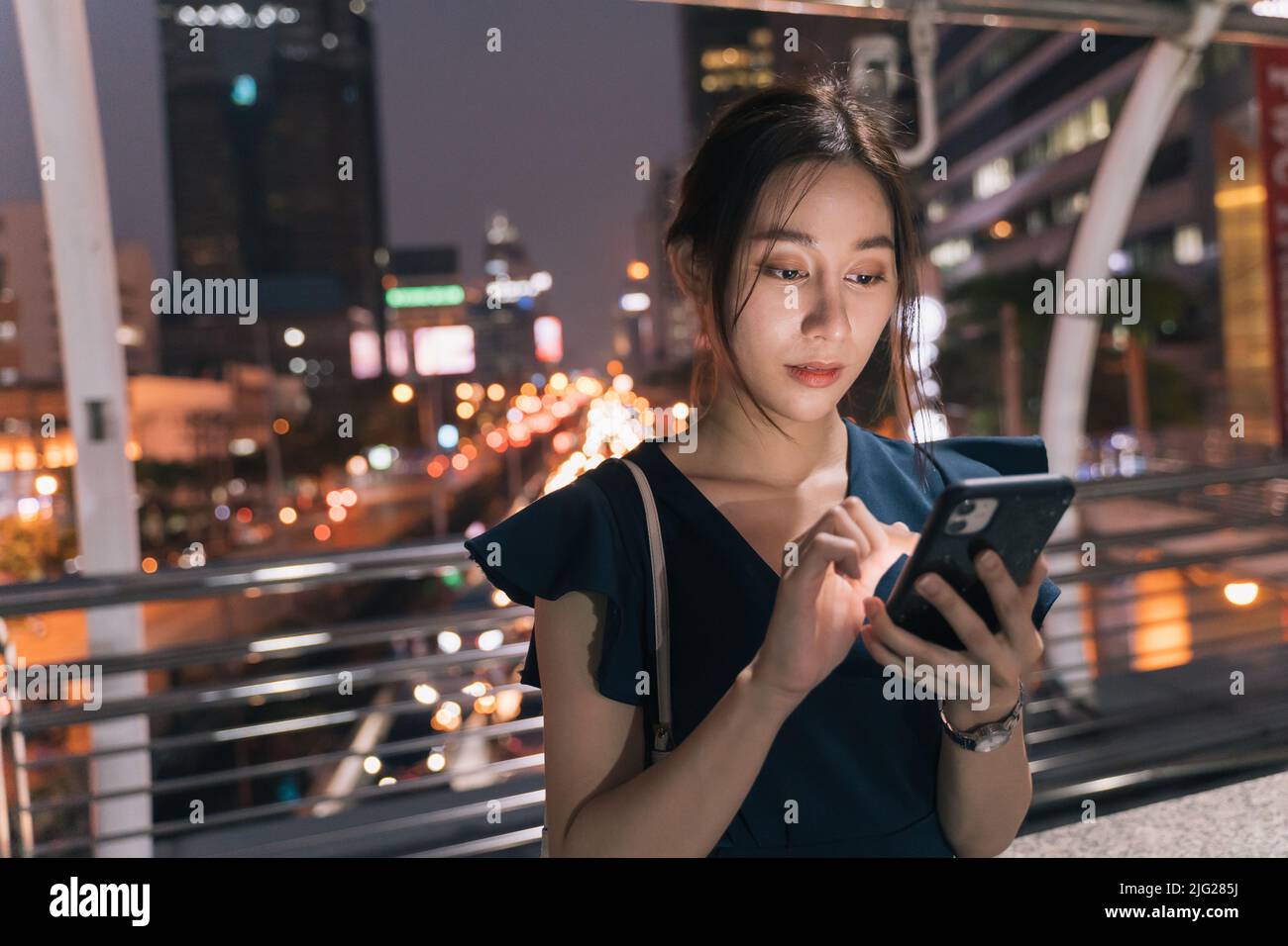 Beautiful young Asian woman standing over footbridge bridge checking smartphone and browsing through apps while checking email Stock Photo