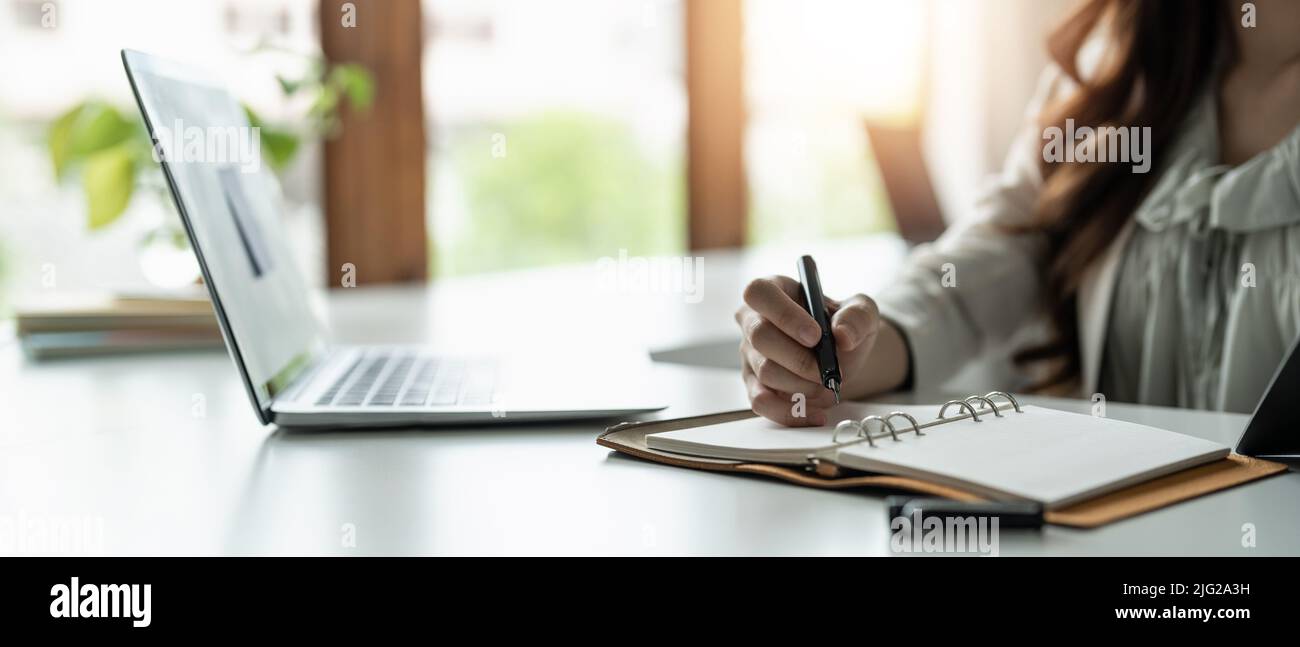 Close up of concentrated female student busy studying using laptop make notes in notebook, focused man worker employee write watching webinar or Stock Photo