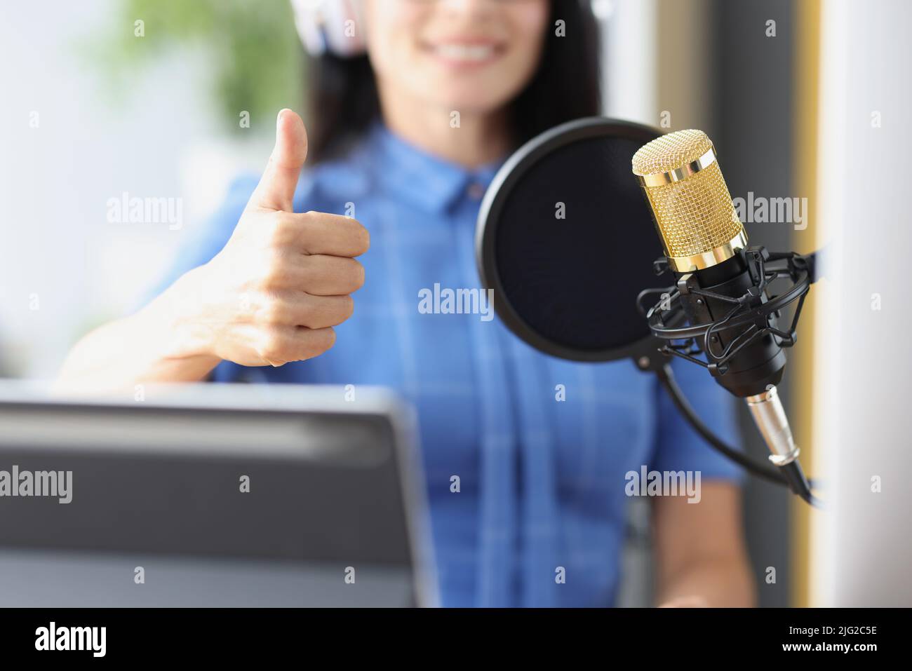 Woman in headphones in front of microphone in studio showing thumb up