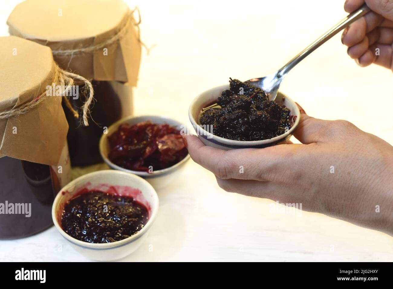 A hand serving homemade mulberry jam in small bowls from jars Stock Photo