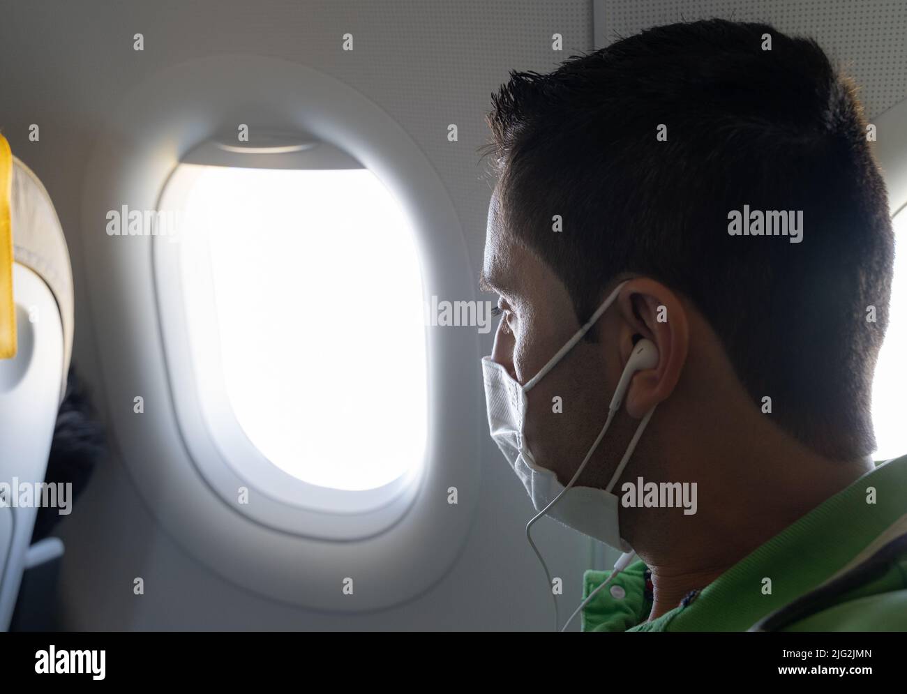 Male passenger with face mask and earphones looking through plane