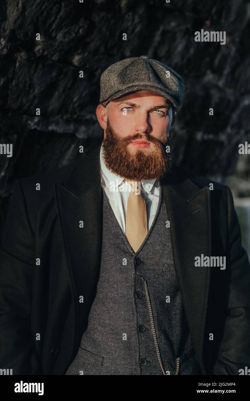 Bearded man with blue eyes  wearing  vintage clothes from the 20s with a brick background Stock Photo