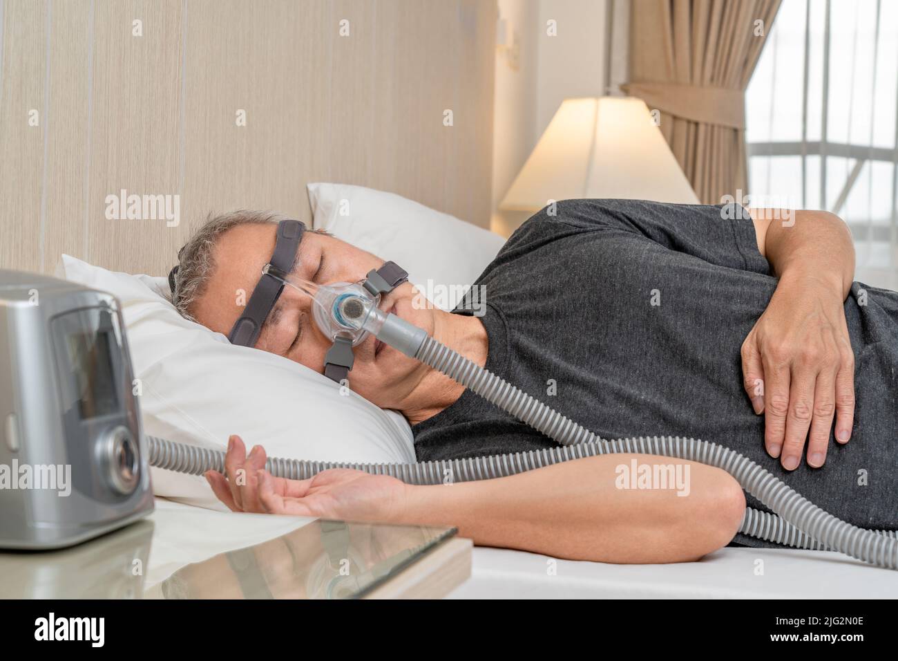 Middle age male with sleep apnea wearing CPAP headgear and mask while sleeping in his bedroom Stock Photo
