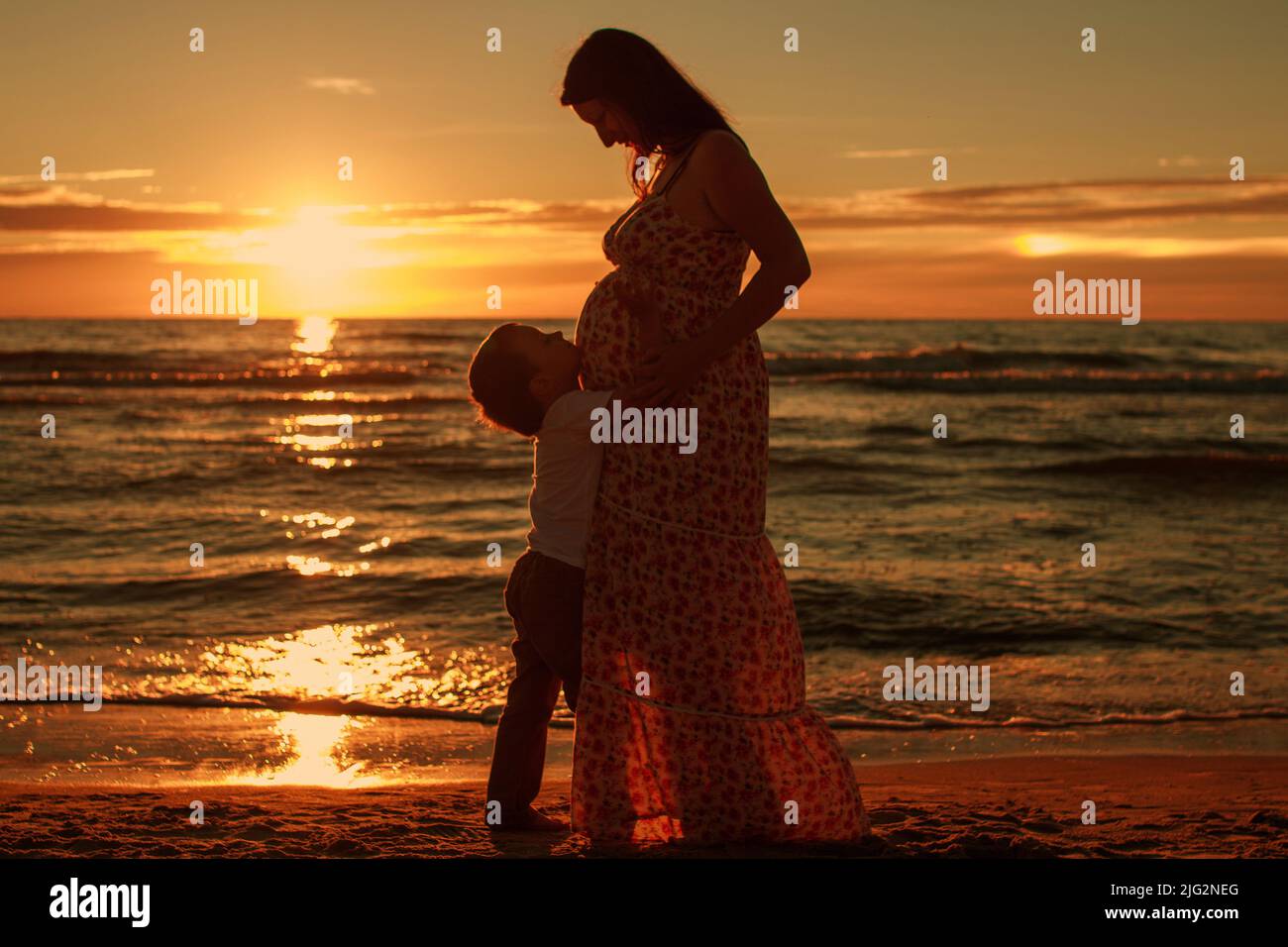 Pregnant woman with a boy on the beach at sunset Stock Photo