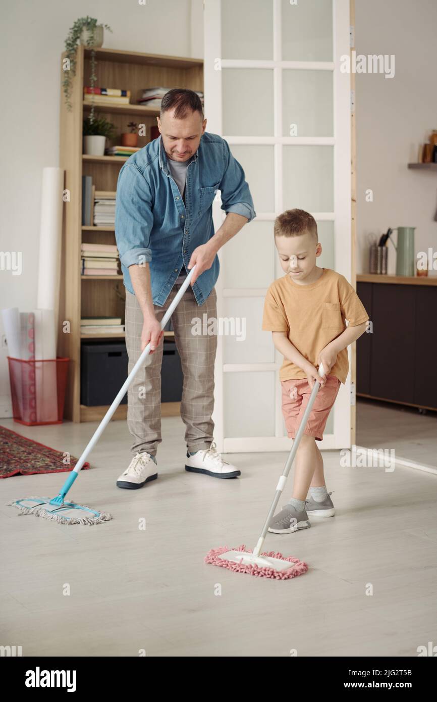 Little son washing floor with mop together with his dad, he helping him
