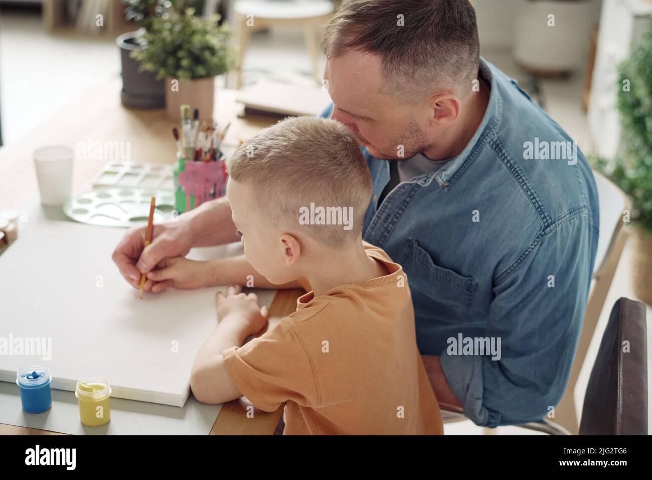 Father teaching his son to paint a picture at table during their leisure time Stock Photo