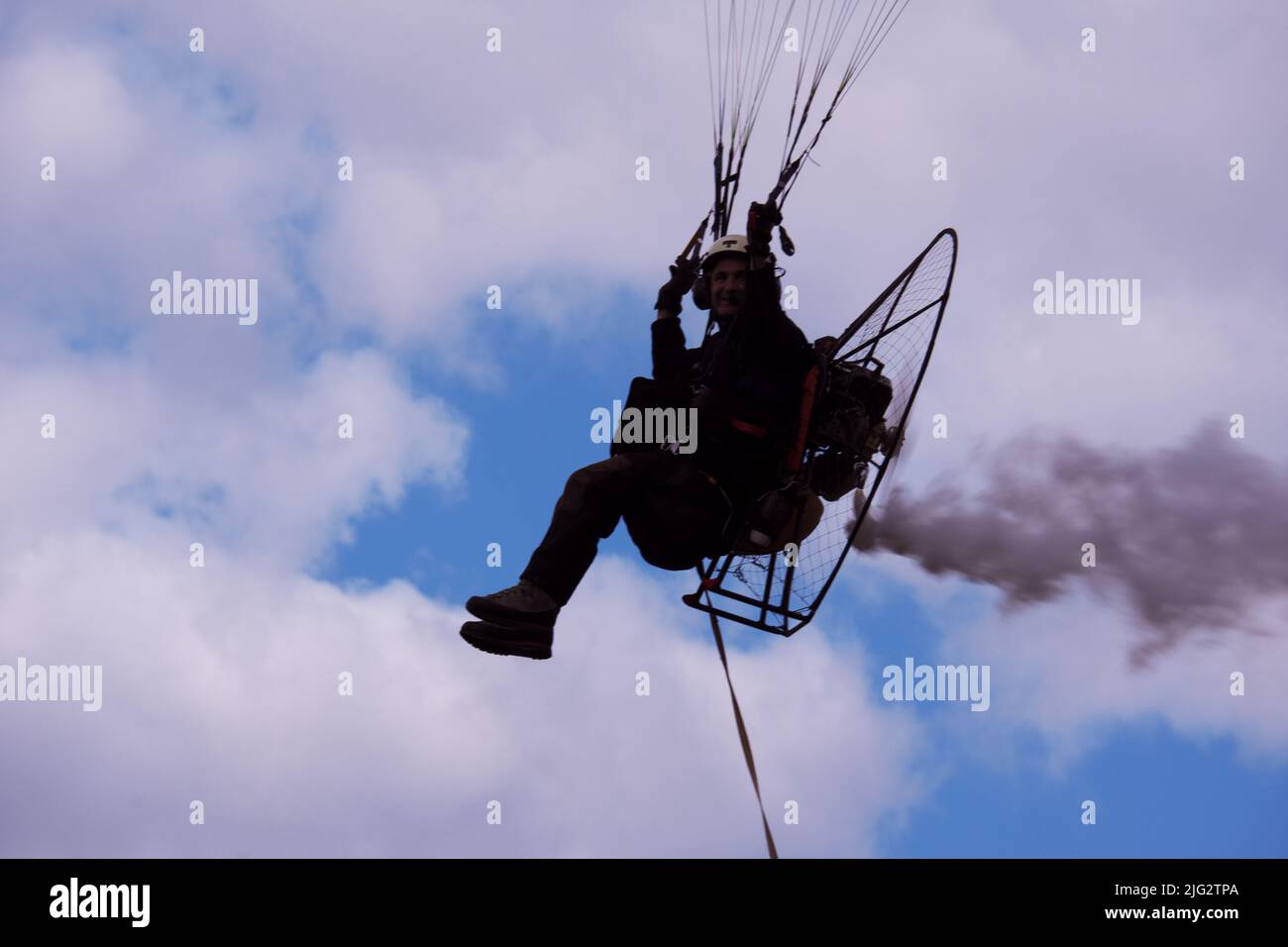 Parachute pilot flying with engine at a cloudy weather with smoke at the back Stock Photo