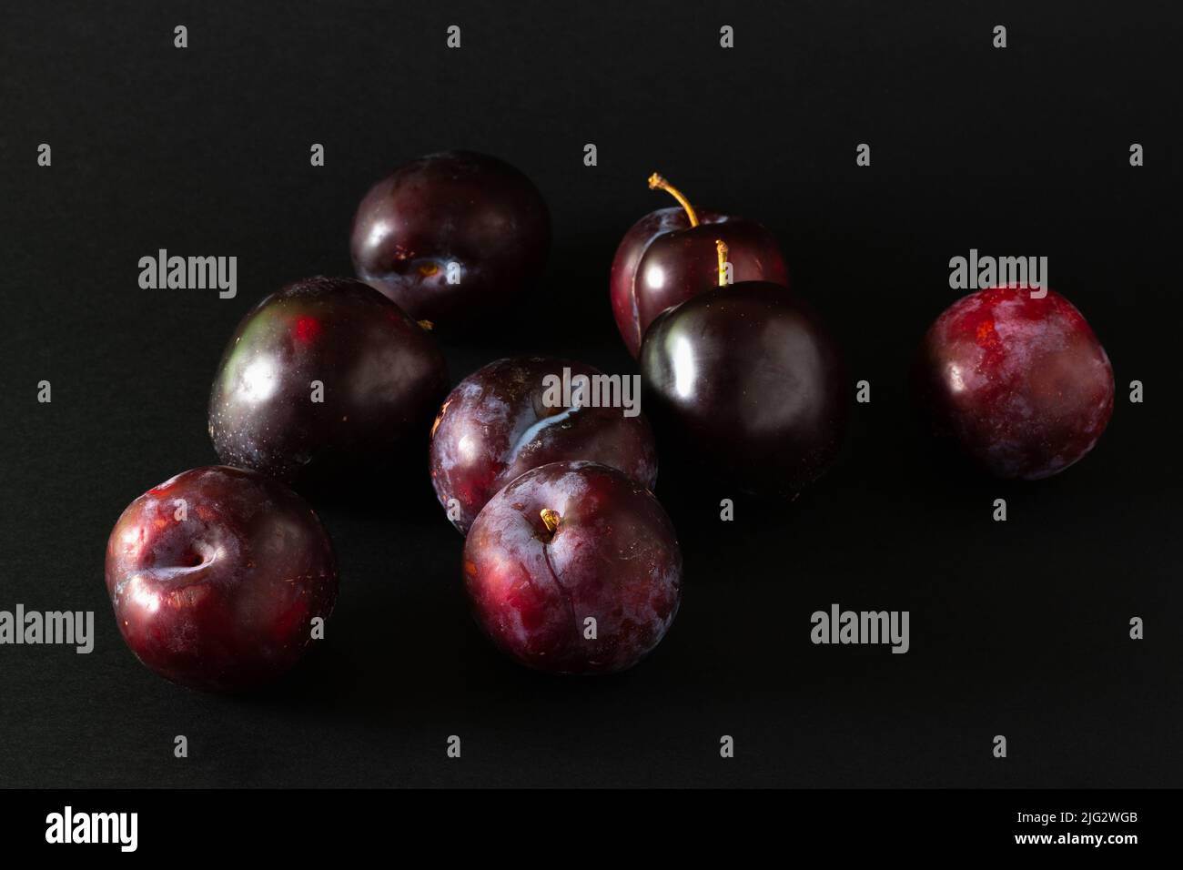 Stack of purple plums on black background. Stock Photo