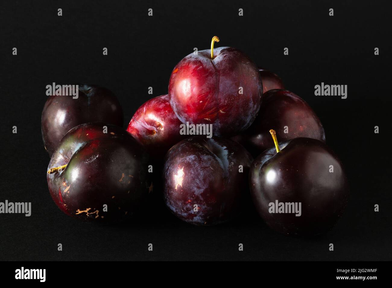 Stack of purple plums on black background. Stock Photo