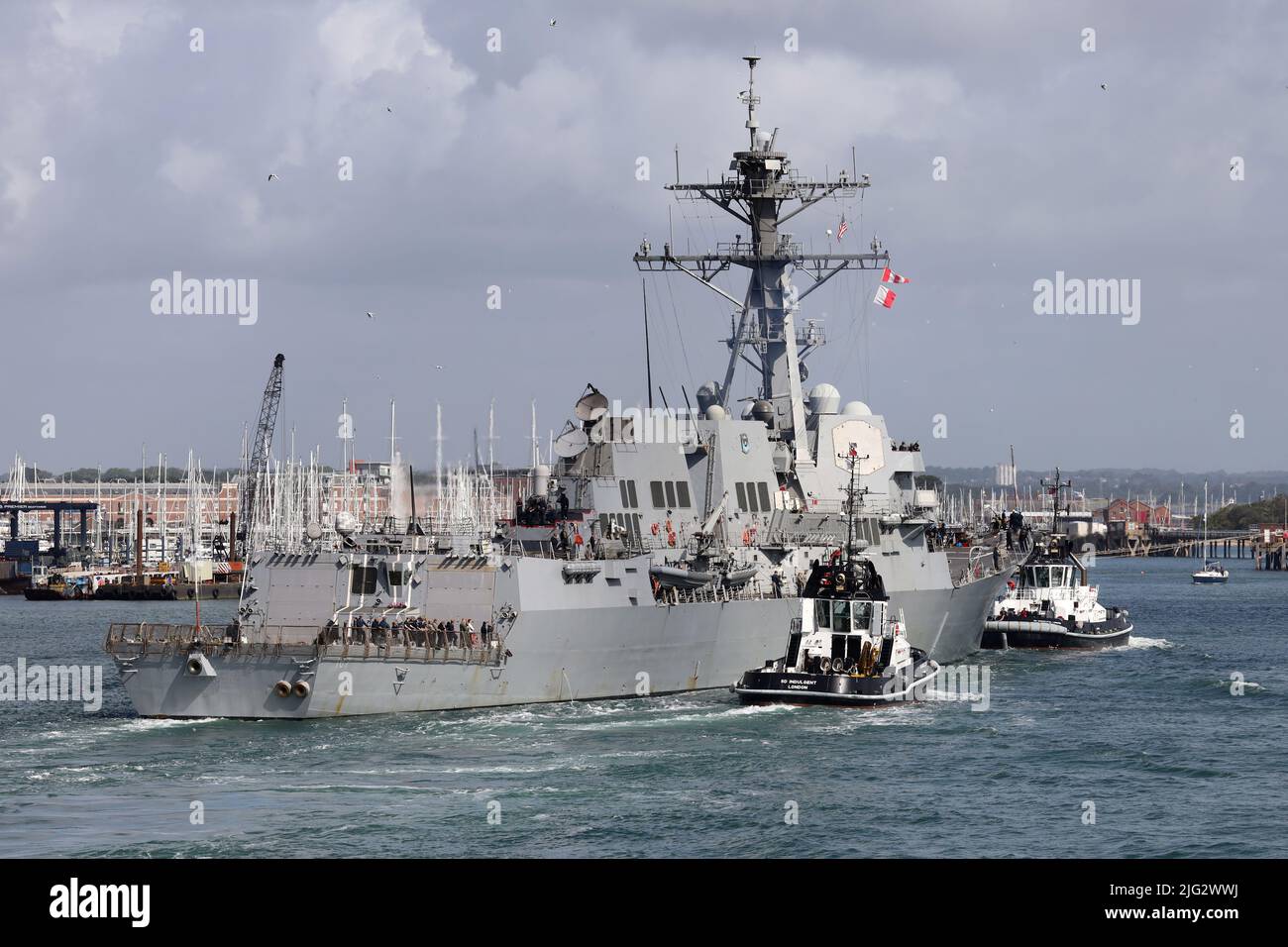 The tugs INDULGENT and BOUNTIFUL escort the US Navy guided missile destroyer USS GRAVELY towards a berth in the Naval Base Stock Photo