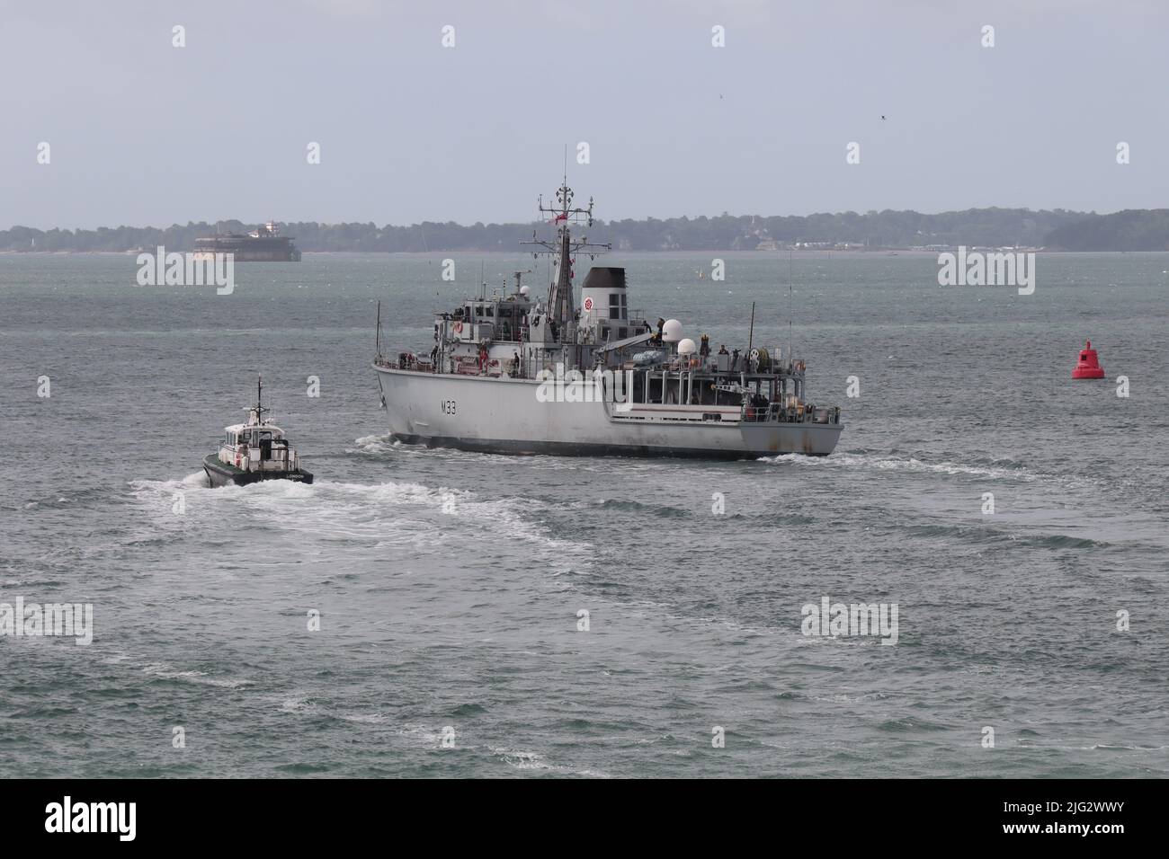 HMS BROCKLESBY changes course as it leaves harbour and heads into The Solent escorted by an Admiralty pilot launch Stock Photo