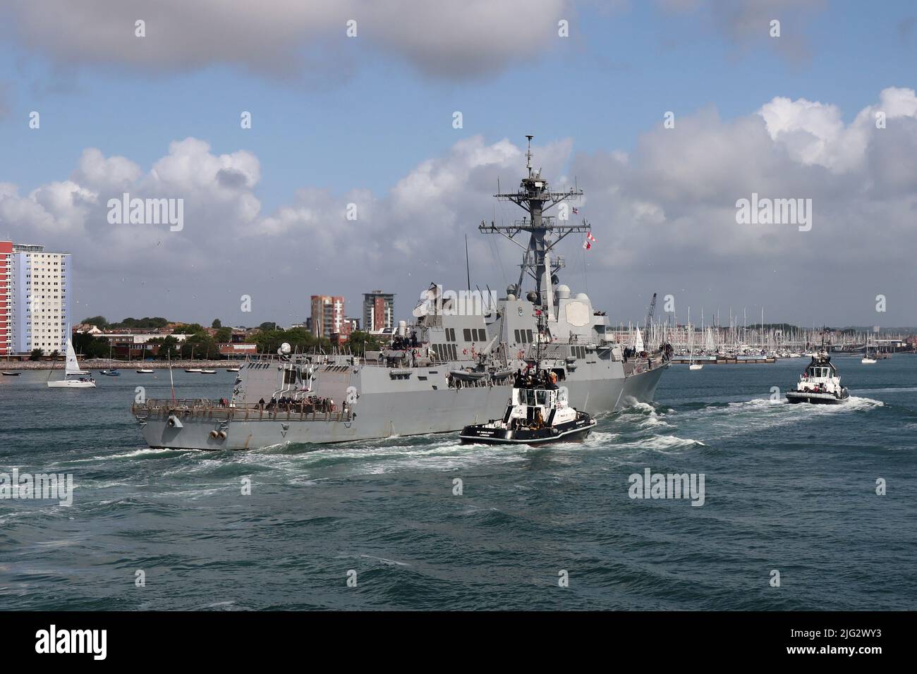 The tugs INDULGENT and BOUNTIFUL escort the US Navy guided missile destroyer USS GRAVELY towards a berth in the Naval Base Stock Photo