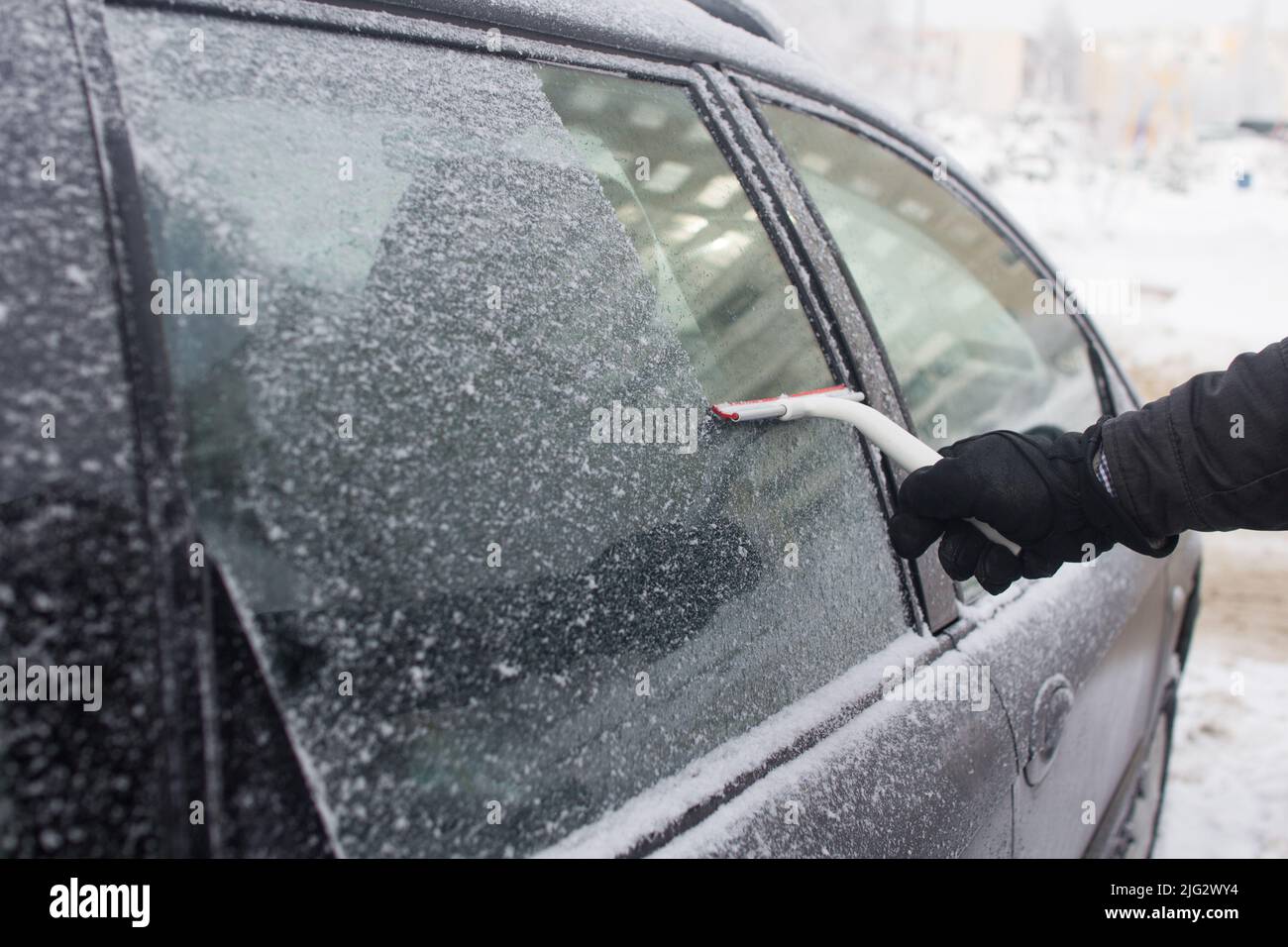 man cleans snow from car window Stock Photo