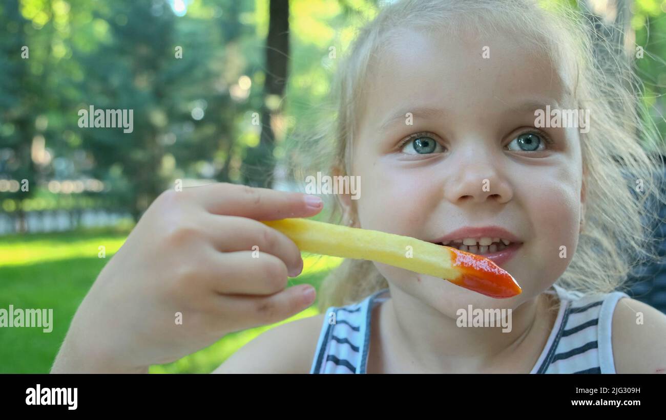 Little girl eat french fries. Closeup of blonde girl takes potato