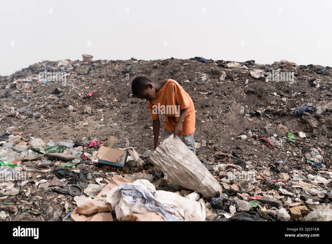 Street boy filling a plastic bag with reusable items found at a landfill site in a West African capital to make a living; symbol of stolen childhood Stock Photo