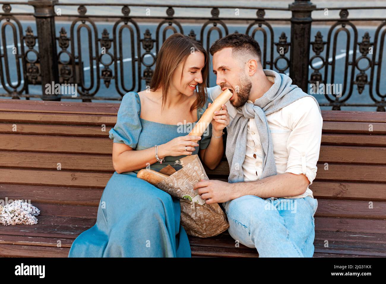 Couple sitting on the park bench and eating sandwich , having fun outdoors. Dating, lifestyle concept Stock Photo