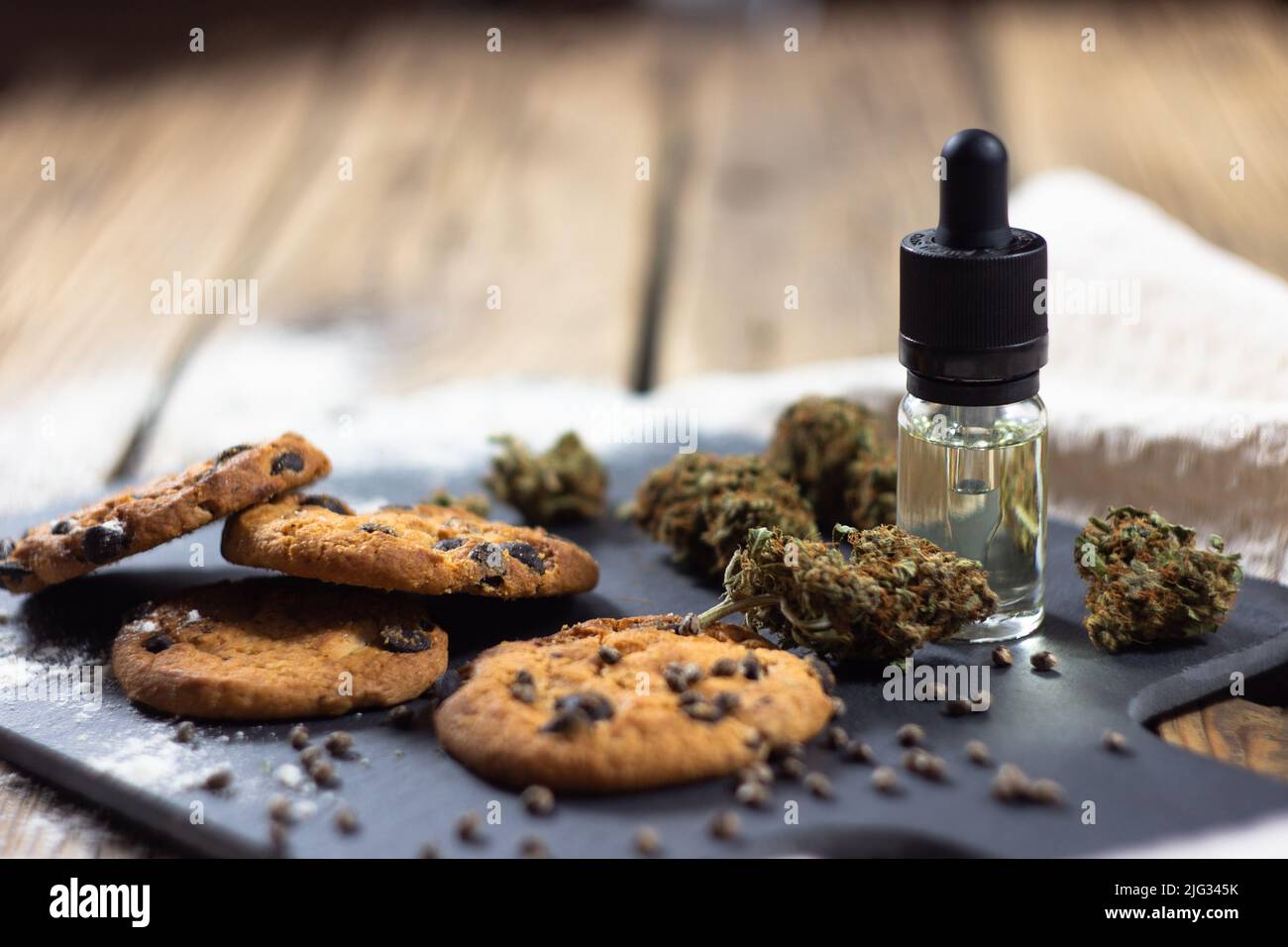 Homemade chocolate chip cookies with cbd oil, surrounded by dry cannabis buds, marijuana seeds and a glass bottle with a dropper of cbd oil. Stock Photo