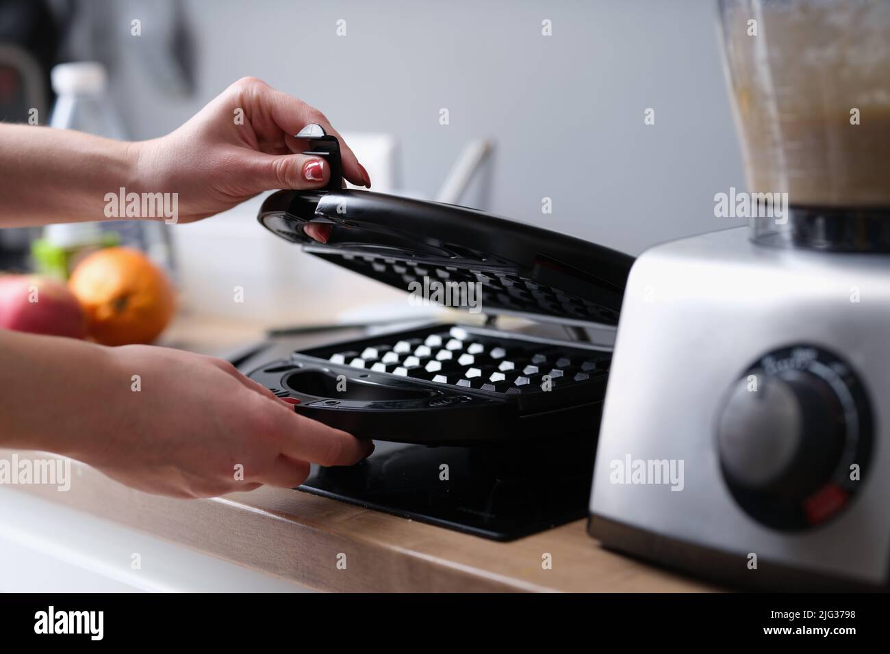 Woman opens electric waffle iron in kitchen Stock Photo Alamy
