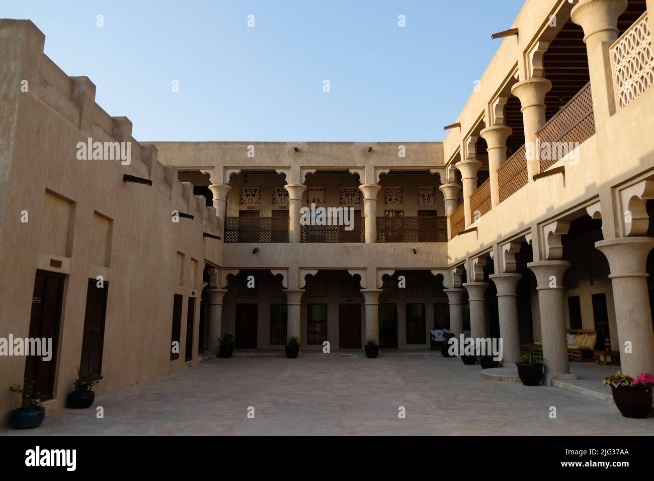 Open and airy courtyard of a traditional Arabic house during the day. Two floors with sand-colored walls and pillars. Clear skies and golden sun. Stock Photo