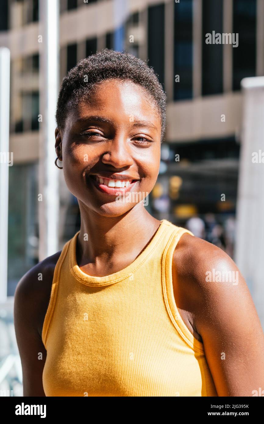 portrait of a cheerful african young woman looking at camera on a sunny day. She wears summer yellow t-shirt Stock Photo