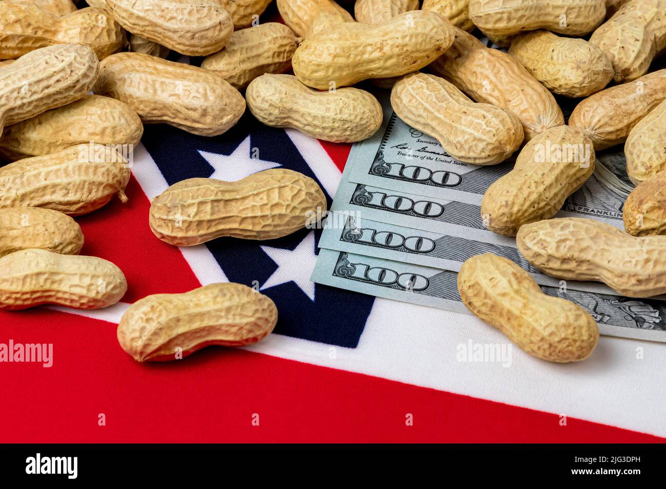 Peanuts in shell on flag of Mississippi with 100 dollar bills. Peanut farming, trade, tariffs and market price concept. Stock Photo