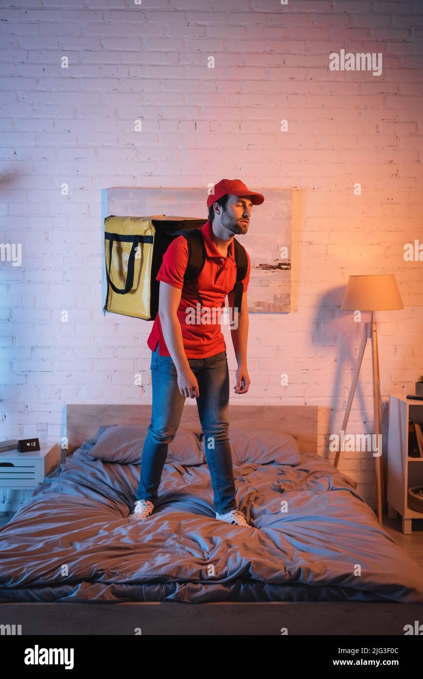 Deliveryman in uniform standing on bed while suffering from sleepwalking at night Stock Photo