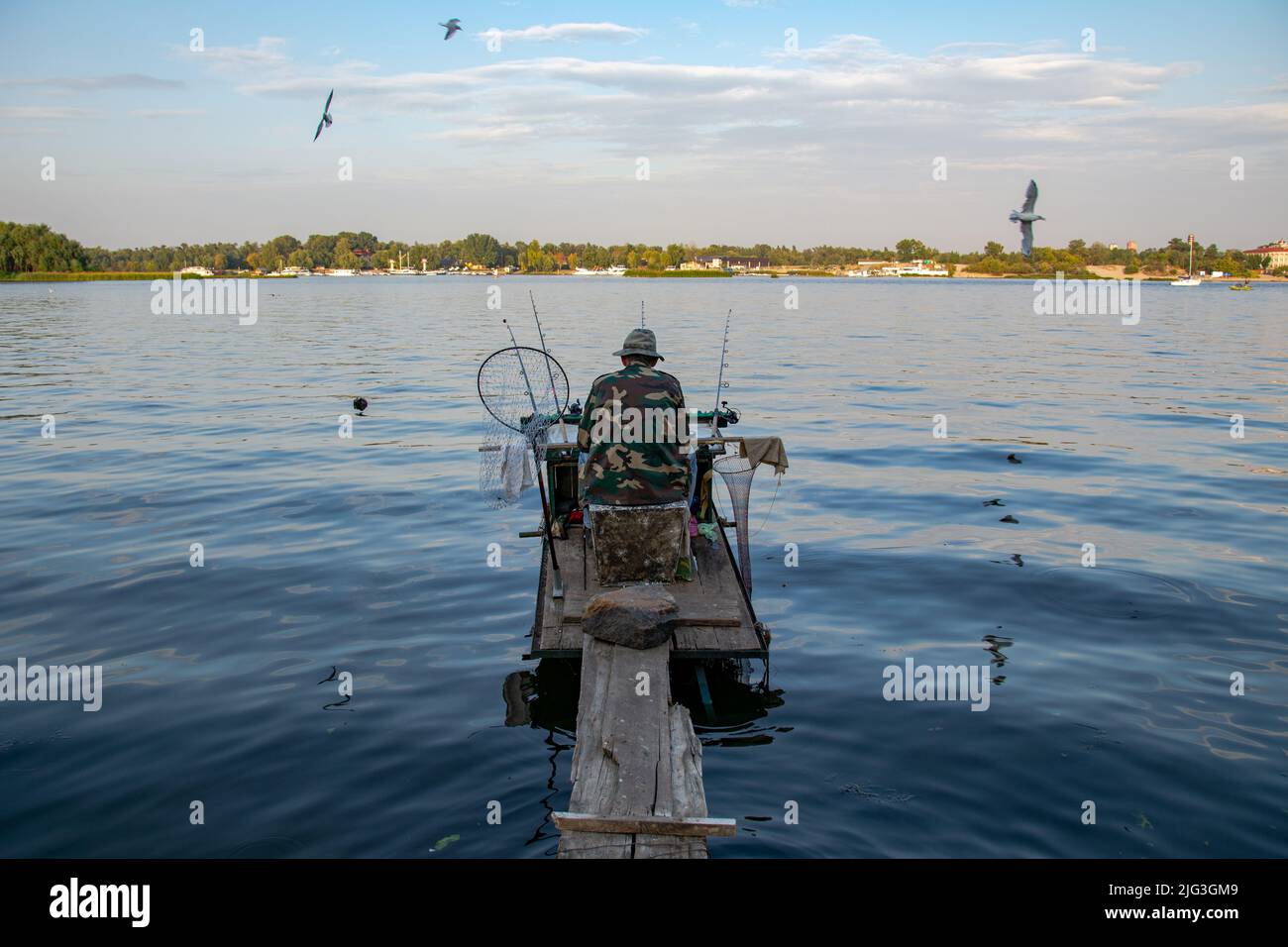 https://c8.alamy.com/comp/2JG3GM9/the-fisherman-sits-on-the-river-on-the-pier-relaxes-and-enjoys-fishing-back-view-of-fisherman-with-a-lot-of-fishing-rods-and-a-net-for-fish-fishing-2JG3GM9.jpg