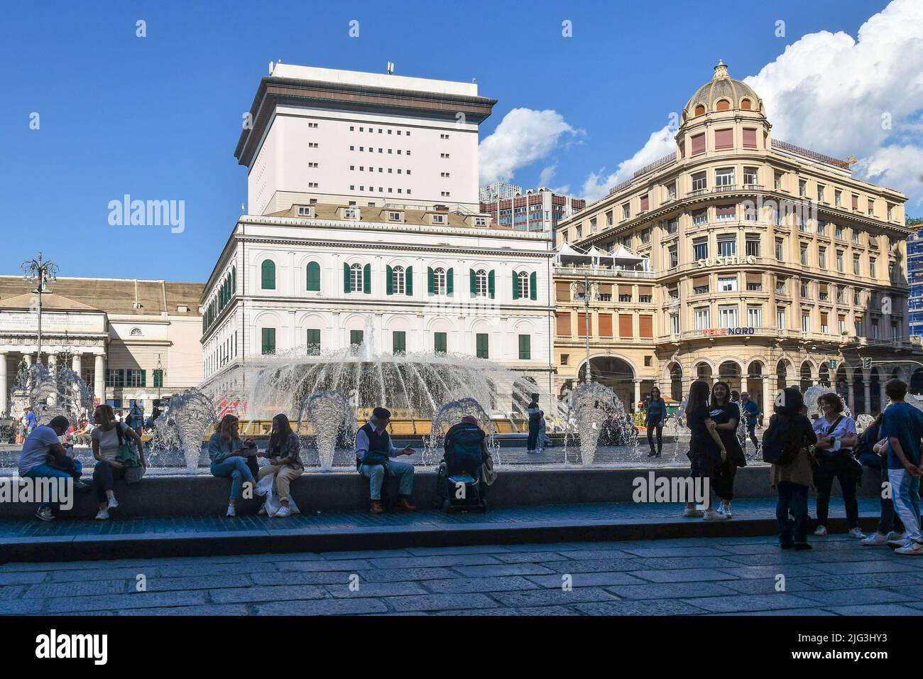 Tourists sitting on the edge of the fountain in Piazza De Ferrari with the Carlo Felice Theatre and the Ligurian Academy of Fine Arts, Genoa, Liguria Stock Photo