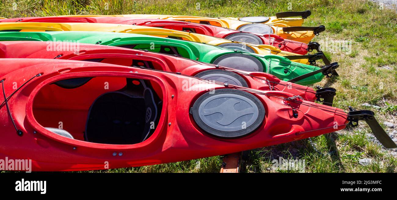 Red, Yellow, Green Kayaks pulled up in a line Stock Photo