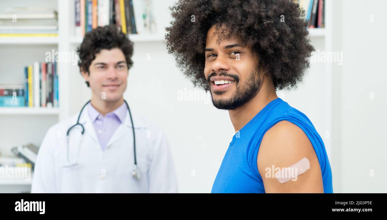 Laughing african american man with doctor after vaccination against Covid 19 as protection against coronavirus Stock Photo