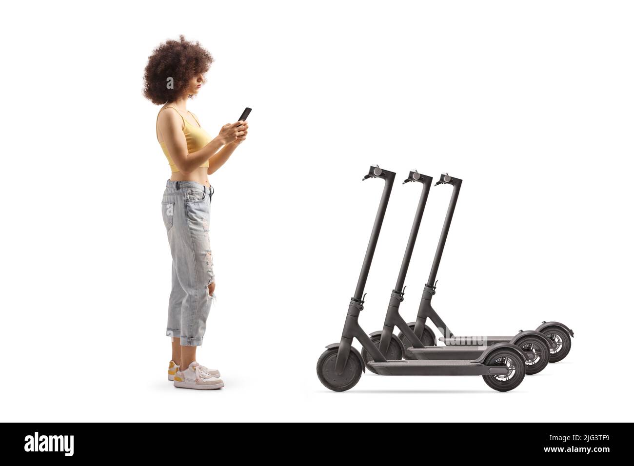 Full length profile shot of a young woman with a curly hair renting an electrical scooter via smartphone isolated on white background Stock Photo