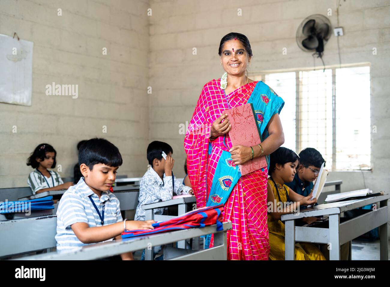 Teacher looking at camera while teaching to elementary school students at classroom - cocept of tutor, professional education and education Stock Photo