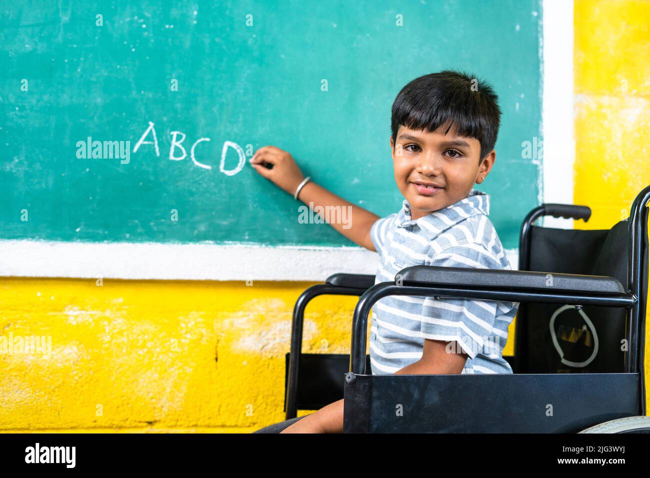 Young teenger school kid with disability on wheel chair writing on board while looking at camera - concept of education, growth and development Stock Photo
