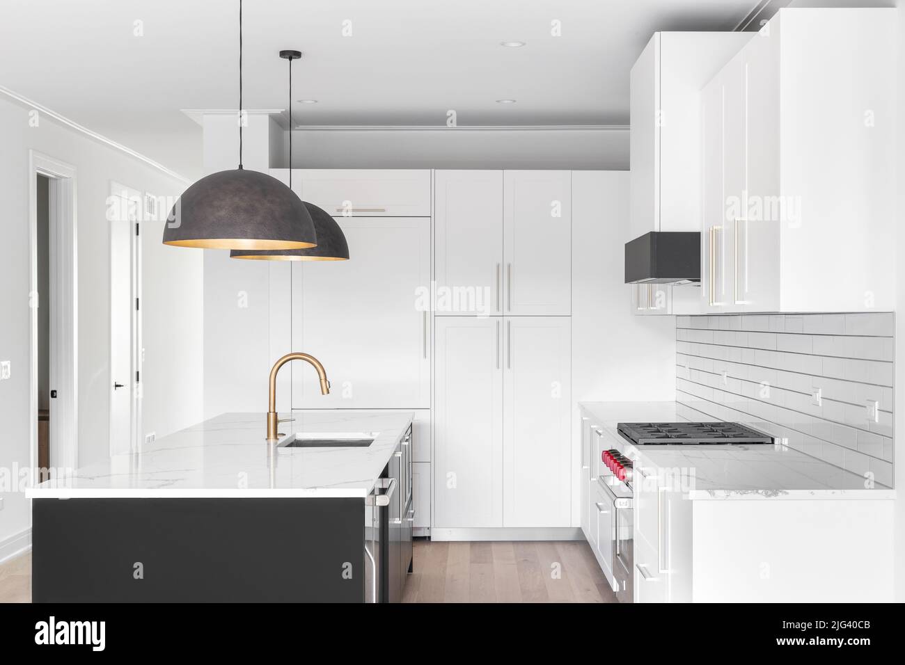 A beautiful, modern kitchen with white cabinets, large pendant lights above a black island, subway tile backsplash, and white marble countertop. Stock Photo