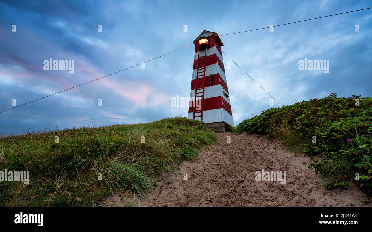 Lighthouse on top of a sand dune with Leymus. A patch of sand leads up to the lighthouse. Taken during the blue hour in Vorupør, Denmark. Stock Photo