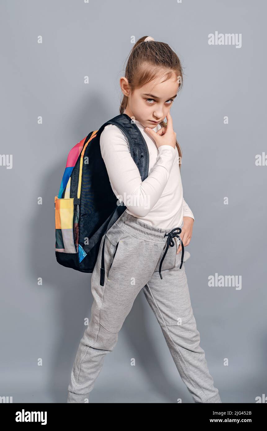 Little girl with backpack. Schoolgirl with backpack looks seriously and frowning. Problems at school. Stock Photo