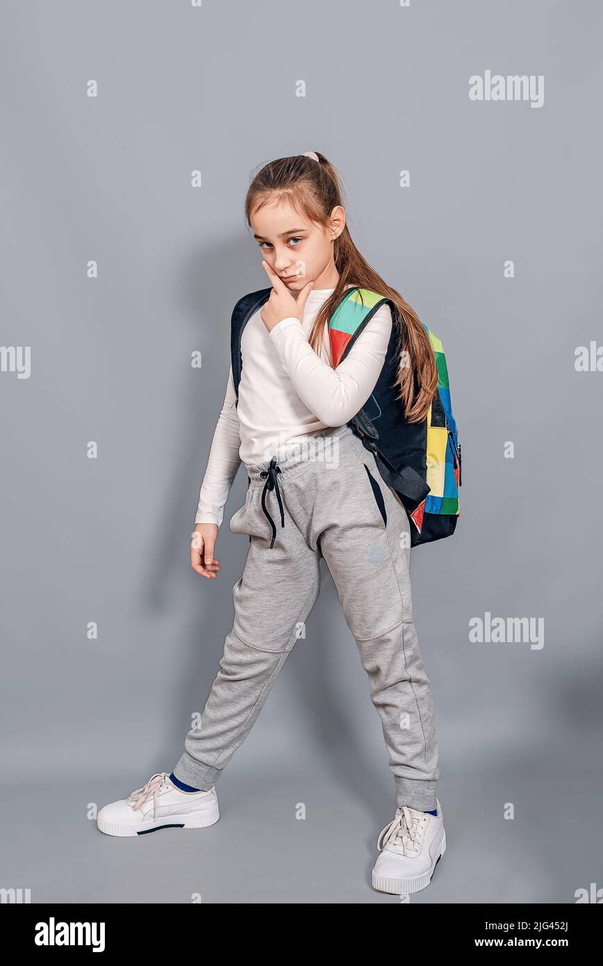 Little girl with backpack. Schoolgirl with backpack looks seriously and frowning. Problems at school. Stock Photo
