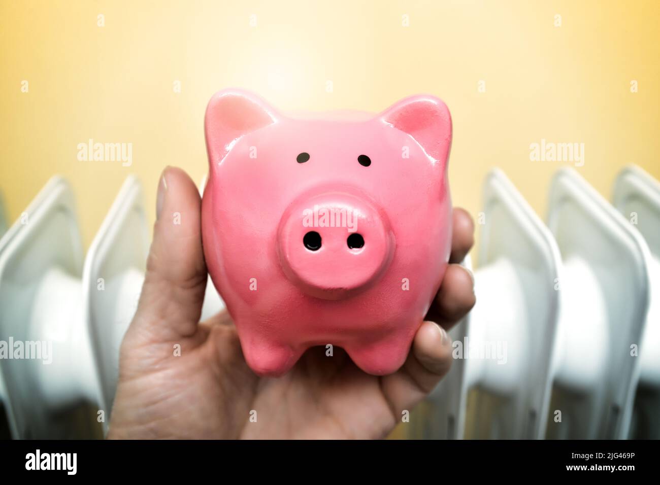 Hand holding a piggy bank in front of a radiator Stock Photo