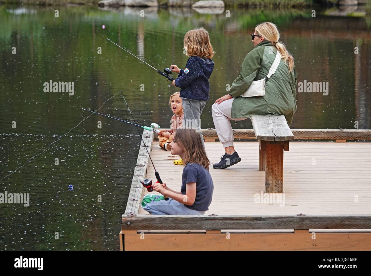 A group of young boys and girls explore and fish around a small pond in early summer in Bend, Oregon. Stock Photo
