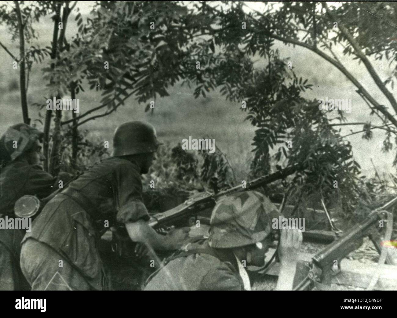 MG-34 machine gun stall. Three divisionaries in a trench with a light machine gun shot MG-34, a fourth character observes with prismatic, carrying a subfusil MP 40. They carry a helmet M 35, two of them with adjustable fabric covers. Stock Photo