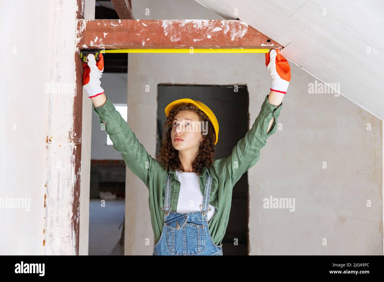 Live portrait of young woman, builder wearing helmet using different work tools at a construction site. Gender equality, job, work concept Stock Photo