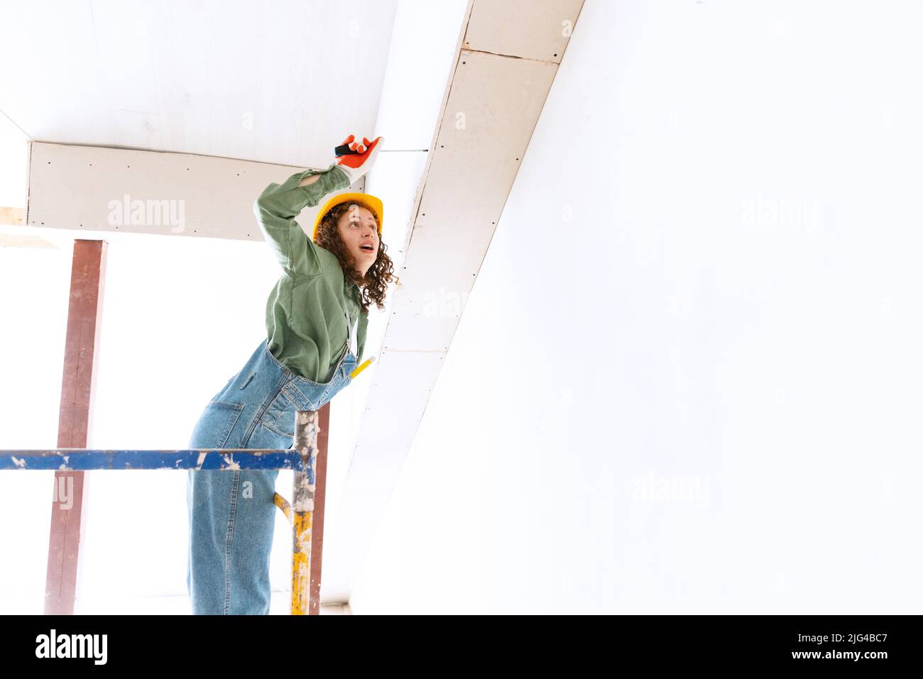 Live portrait of young woman, builder wearing helmet using different work tools at a construction site. Gender equality, job, work concept Stock Photo