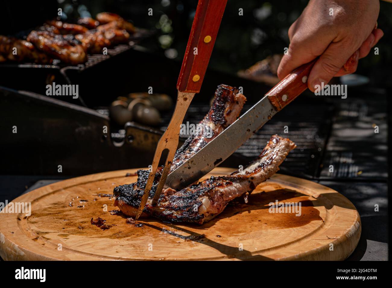 Hand cutting meat with knife and fork. Grilled ribs on the barbecue in summer. Preparaton of food. Stock Photo