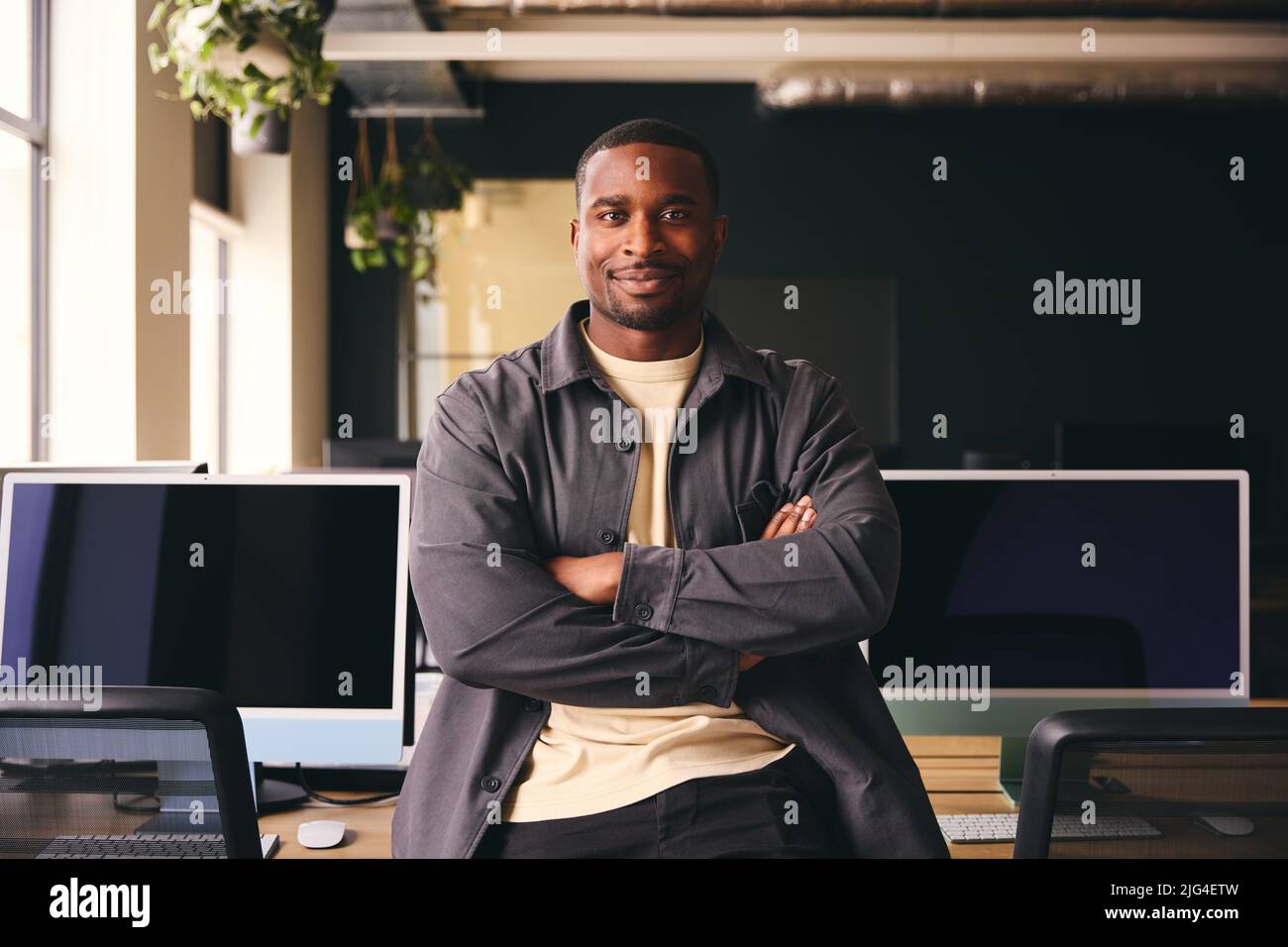 Smiling Young Black Male Standing In Office Looking At Camera With Arms Crossed Stock Photo