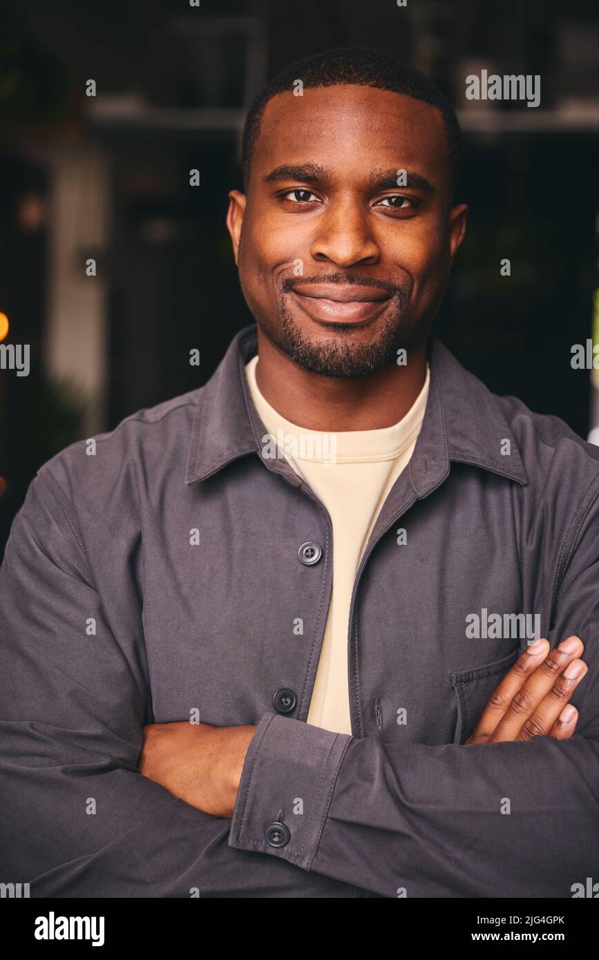 Smiling Young Black Male Standing In Office Looking At Camera With Arms Crossed Stock Photo