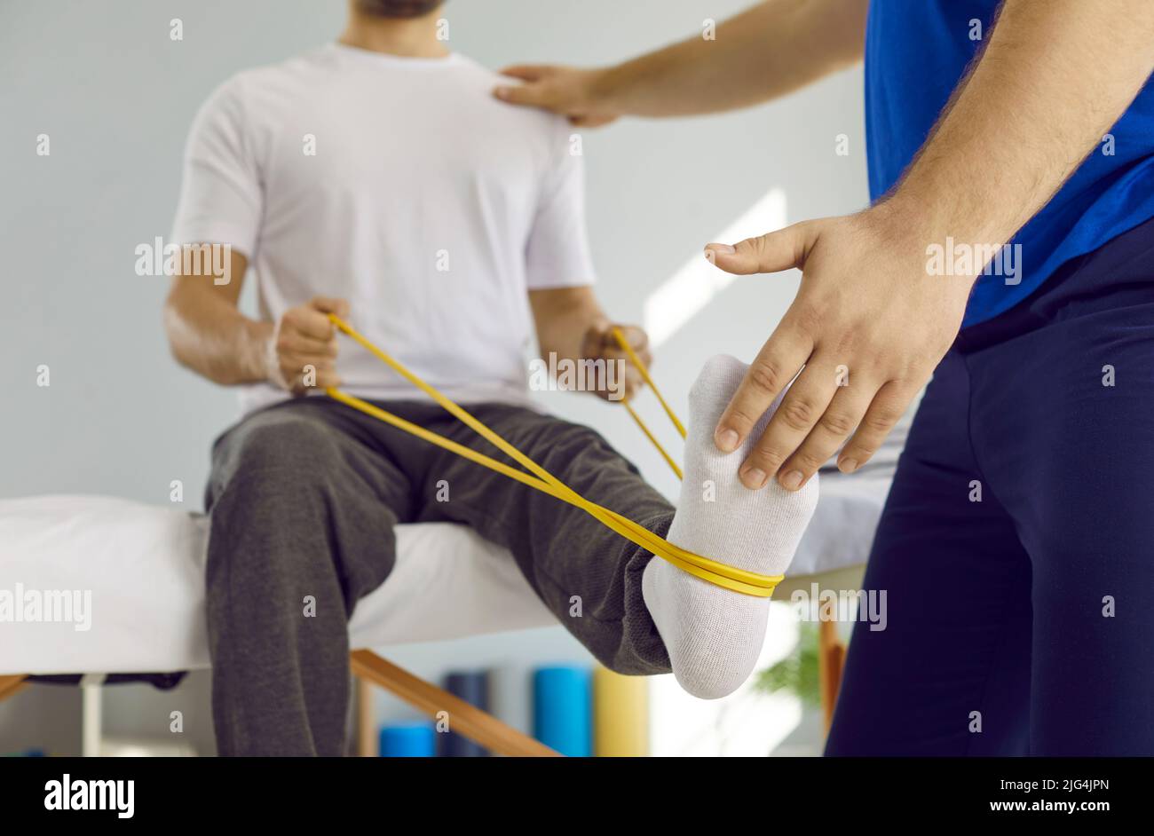 Man doing physical exercises with elastic band at physiotherapy and rehabilitation clinic Stock Photo