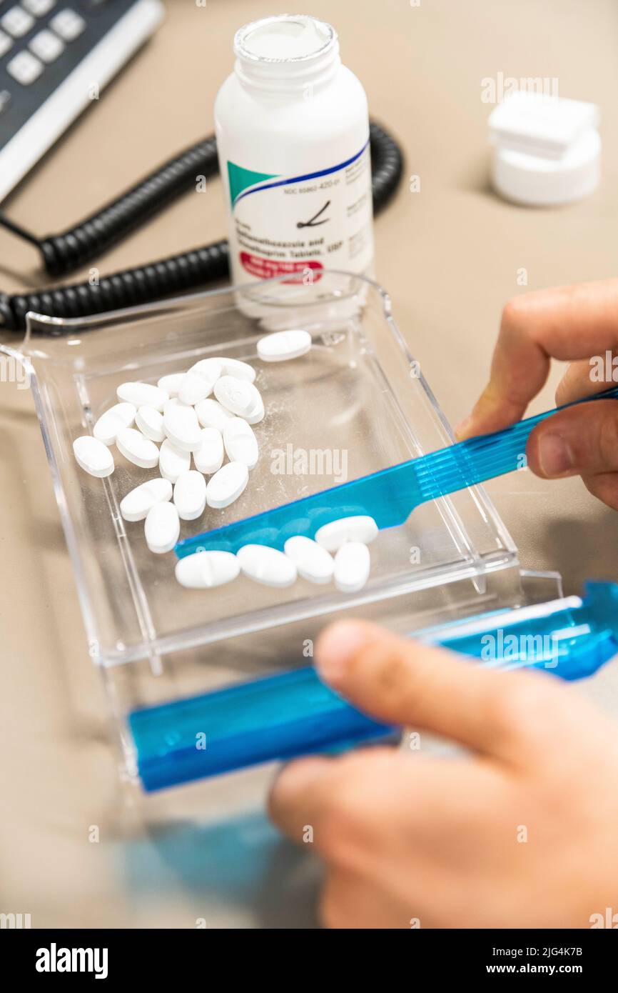 A pharmacists's hands count white pills into a plastic tray at a pharmacy counter Stock Photo