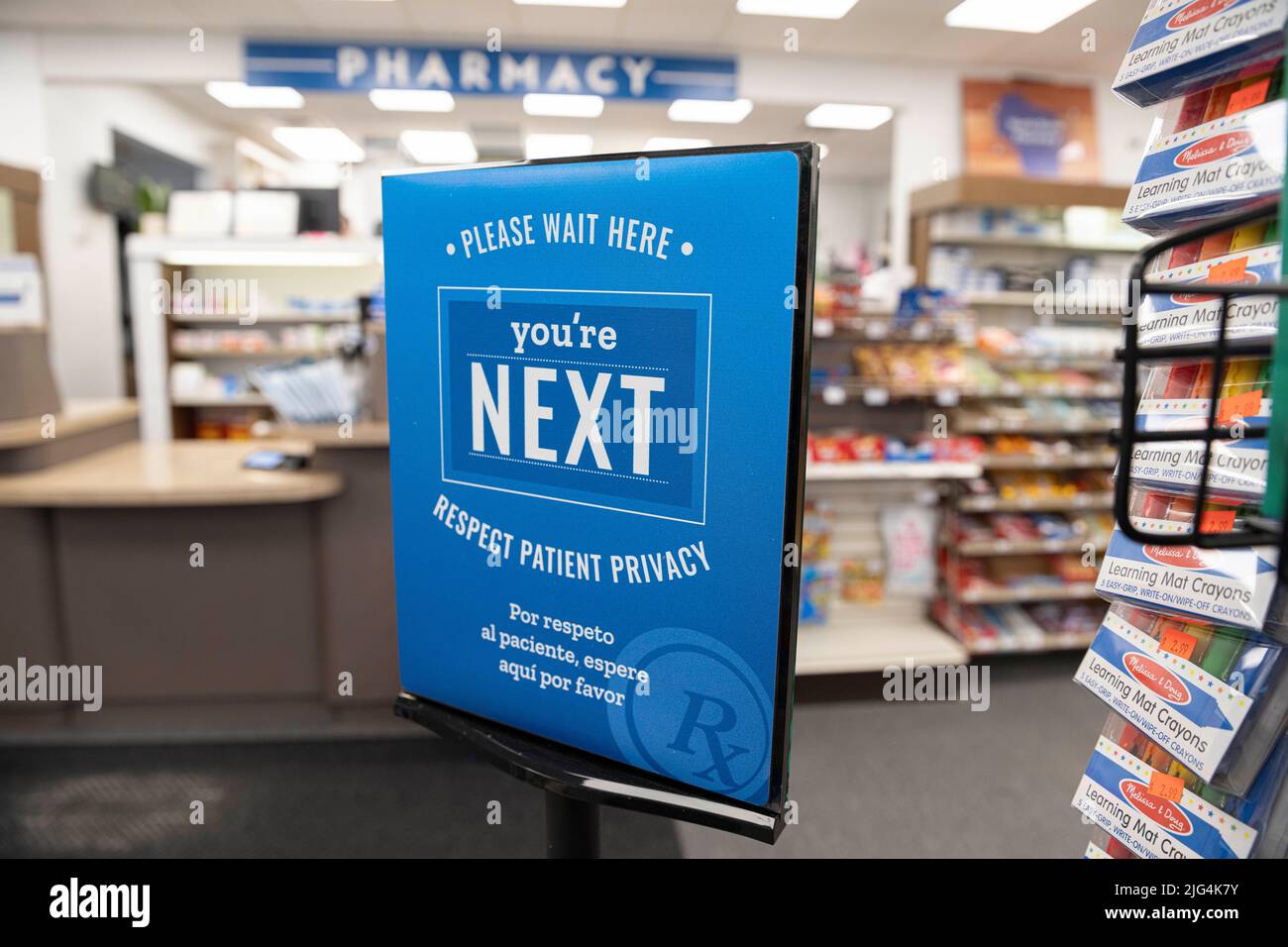 A sign for customers to wait in line stands in front of a small town pharmacy inside a drug store Stock Photo