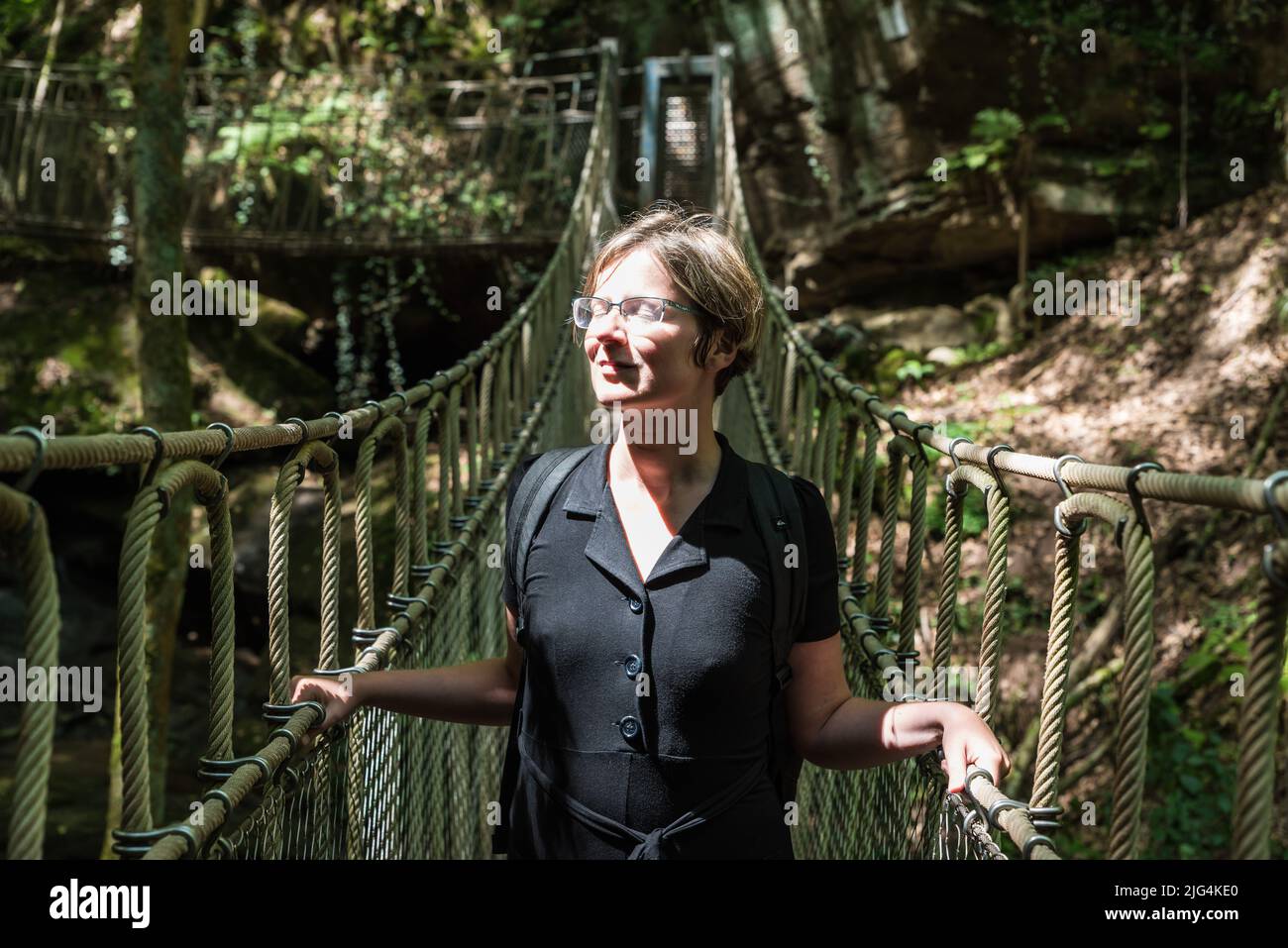 Portrait of a woman at a wooden suspension bridge over a small creek valley in the woods, Kordel, Belgium Stock Photo