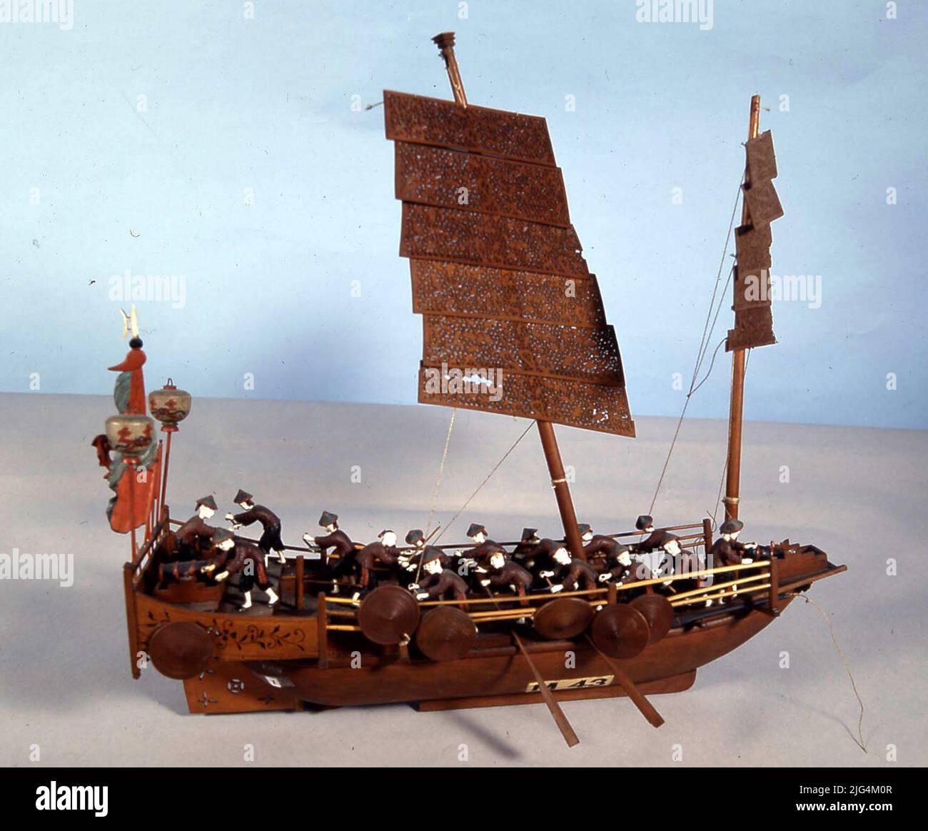 Model The Exvote of Lorcha China (Siglo XIX). Model. Fine, light and little draft vessel. The port and star is longitudinal, some hangers or reeds, somewhat separated from the board, where the shields or paves are hanging. The bow has an open and border platform where an artillery piece is placed. She arbola two sticks with very thin and dragging wooden candles with vegetable motifs divided into horizontal sections. She used to wander and oars. In the stern they have installed two other cannons and on the main terminal lanterns, among which standards or flags that may have religious symbology. Stock Photo